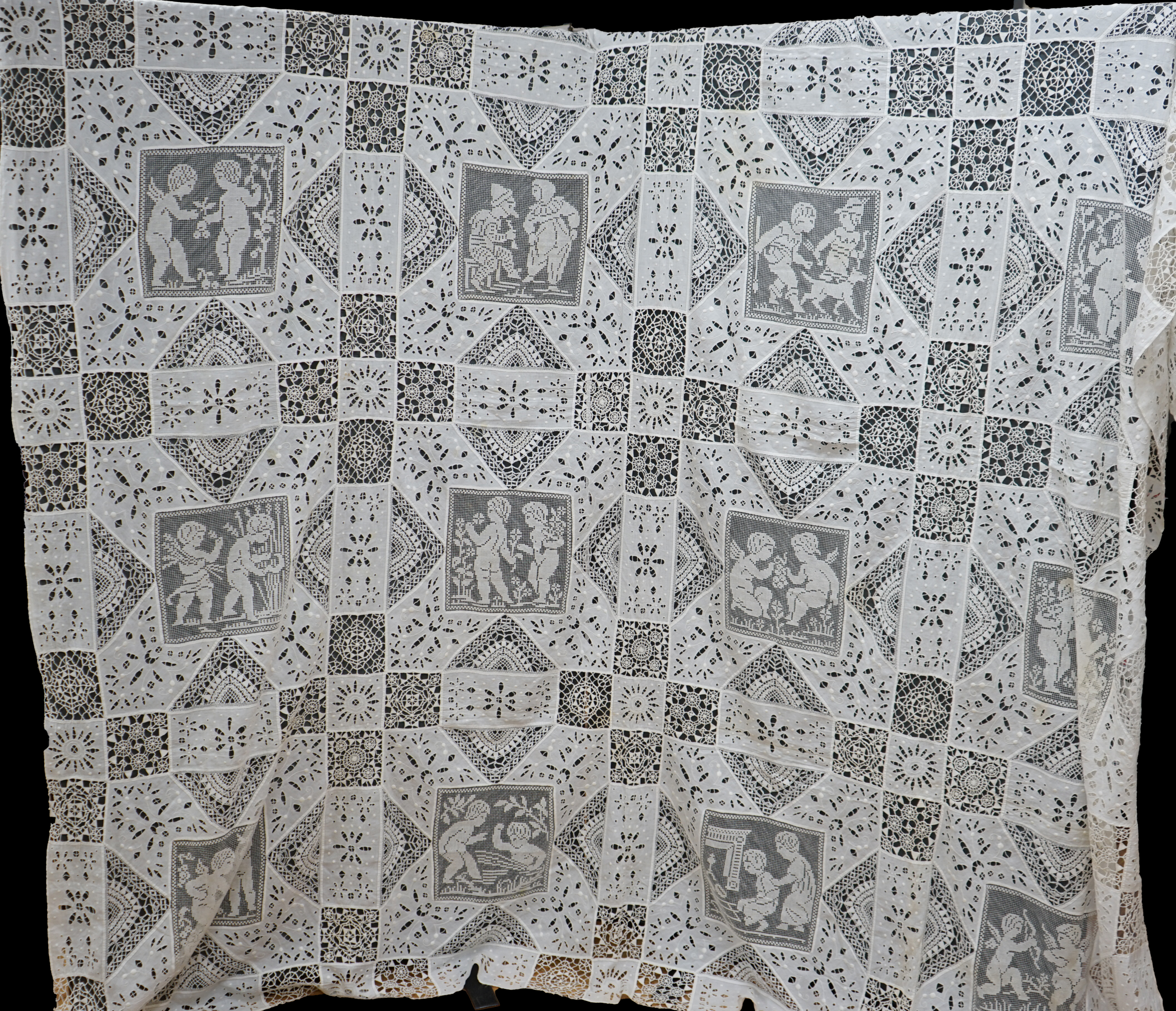 An early 20th century Italian ornate bedcover, worked with square fillet lace insertions of putti, white multi patterned cut work squares on fine linen and similar multi patterned needle lace squares, creating a unique b